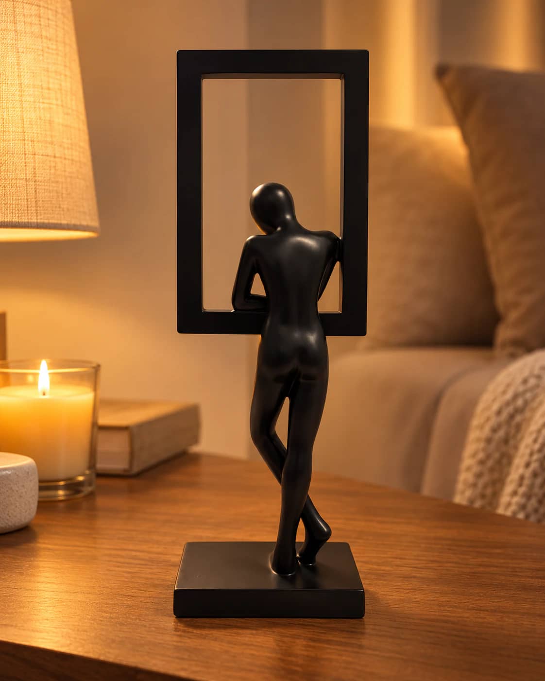 Sculpture noire du penseur dans son cadre, vue de dos, sur un meuble en bois éclairé par une lampe