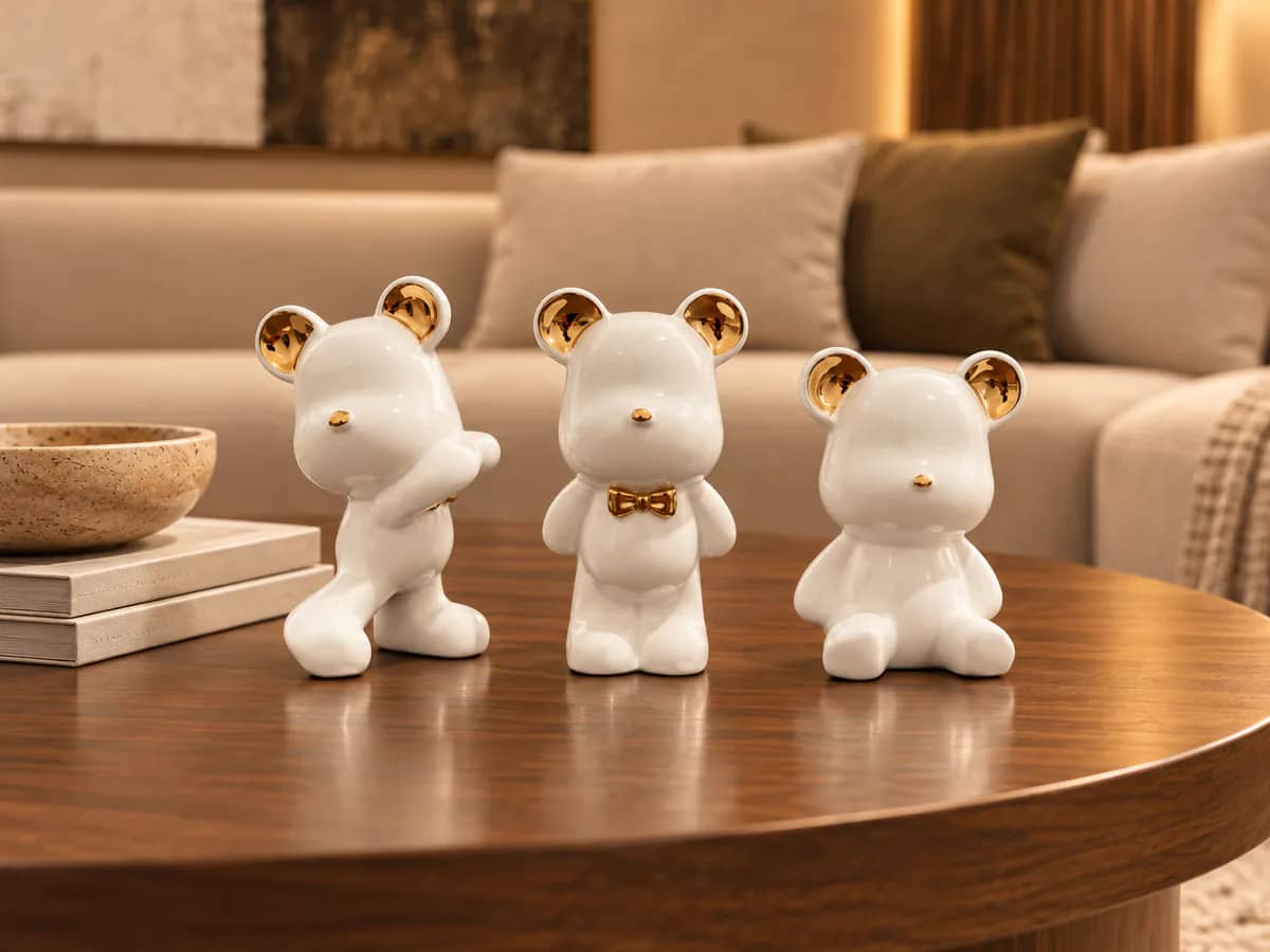 Trio d’ours en céramique blanc et or sur une table basse en bois devant un canapé clair